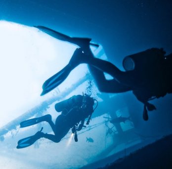 Divers explore the underwater side of a boat.
                  