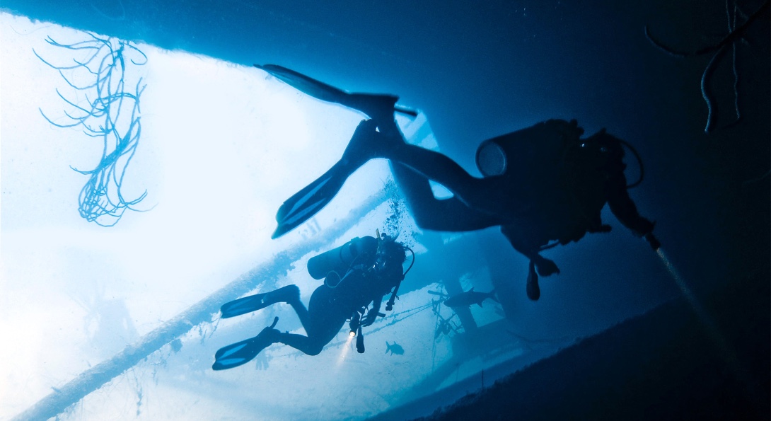 Divers explore the underwater side of a boat.