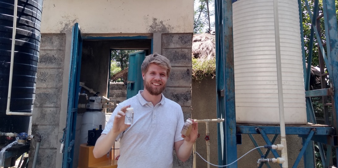 MPH student Colin Hendrickson poses for a photo holding up two vials of water at a water purification station in Kenya.