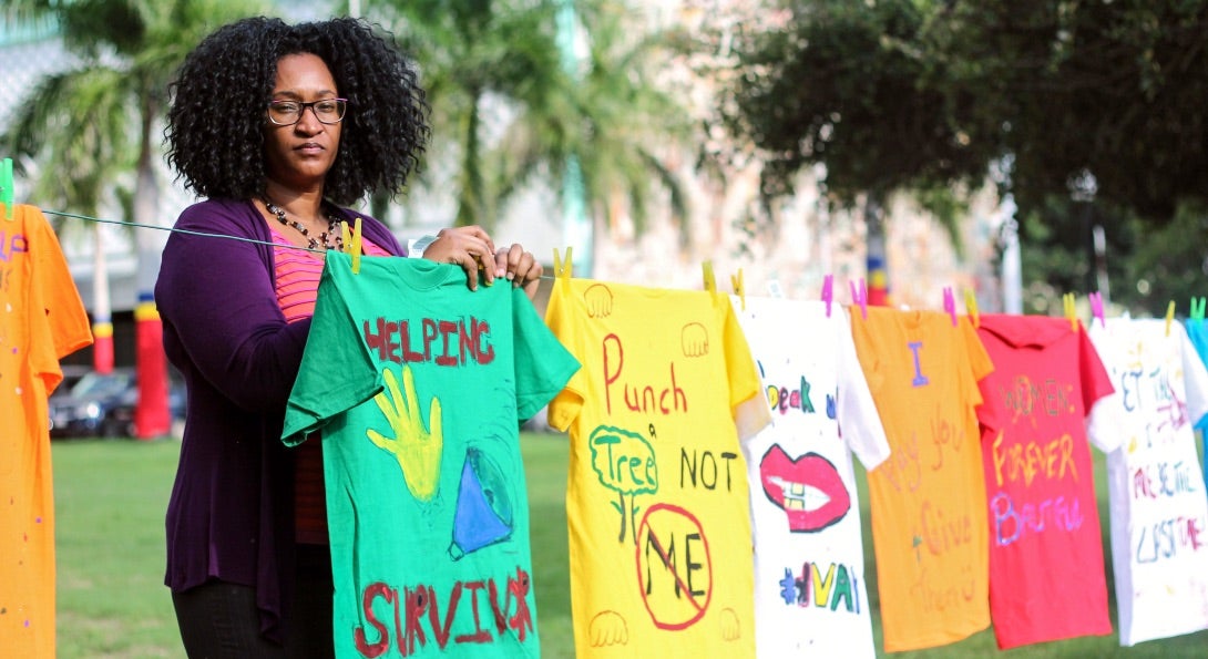 A community-based organization staff worker stands near a series of painted t-shirts that encourage anti-violence.