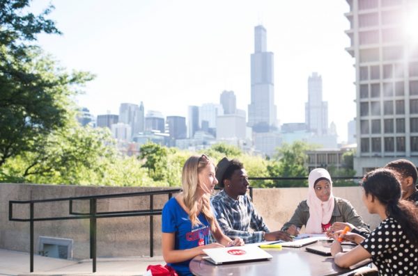 UIC students engage in a group project sitting at a table outdoors atop the BSB building on UIC's campus.