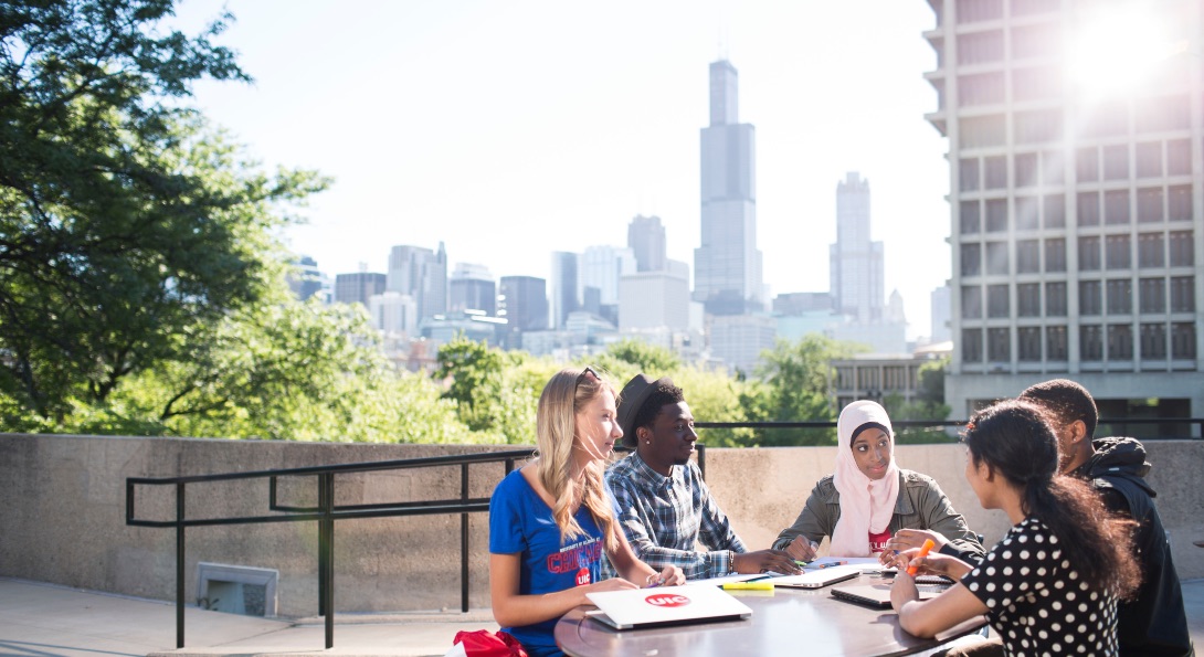 UIC students engage in a group project sitting at a table outdoors atop the BSB building on UIC's campus.