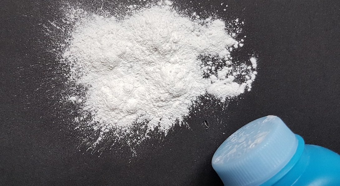 A bottle of baby powder, with some of the white powder spilled on a black tabletop.