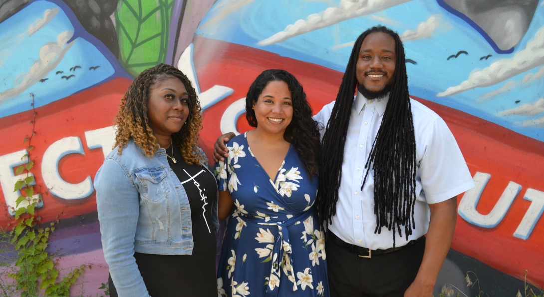 Lawrence Hall staff Narestus Coley, Breanna Hollie and Aaron Brown pose for a photo in front of a mural in the South Shore neighborhood.