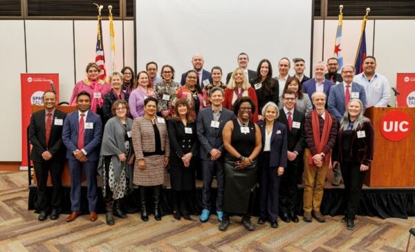 A group photo of all presenters from UIC's January SparkTalks in front of the presentation stage, with Chancellor Miranda.