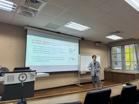 A person speaking in front of a screen showing a Powerpoint slide.