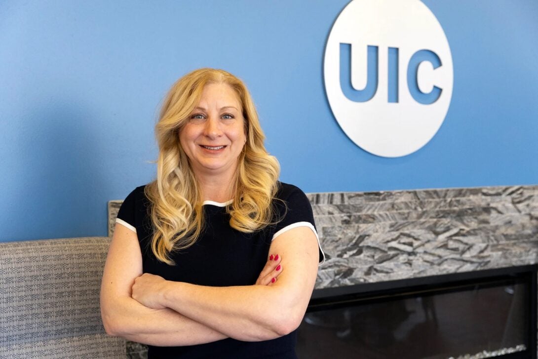 Elizabeth Froelich standing with her arms crossed in front of a light blue wall with the UIC logo