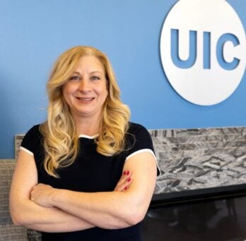 Elizabeth Froelich standing with her arms crossed in front of a light blue wall with the UIC logo 