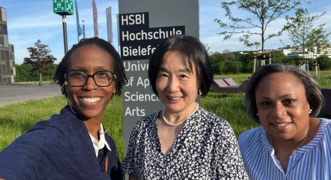 Three professors stand in front of a sign that reads