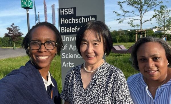 Three professors stand in front of a sign that reads 